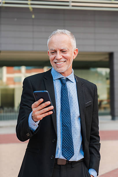 istock Vertical mature businessman with gray hair, using a mobile phone to send work emails. Corporate male professional browsing the internet with a cellphone app. White collar worker with a smartphone 2226377618