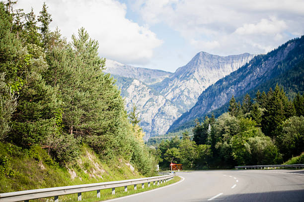 istock Scenic alpine road curving through forest with majestic mountain background 2226377725