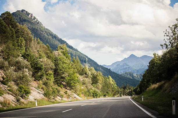 istock Scenic alpine road curving through forest with majestic mountain background 2226377735
