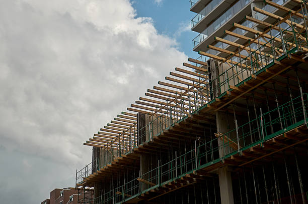 Modern building under construction using wooden scaffolding against a cloudy sky