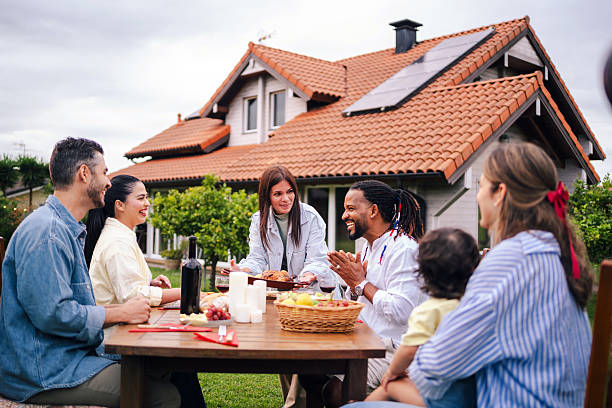 Diverse friends sharing meal outdoors, sustainable home with solar panels creating welcoming backyard gathering environment