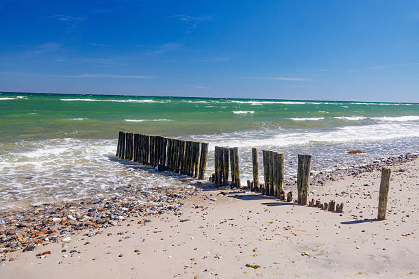 Waves crashing on a wooden groyne protecting a sandy beach from coastal erosion