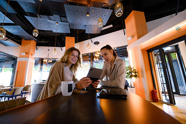 istock Two businesswomen collaborate at a modern cafe, discussing ideas and reviewing documents on a tablet in an inviting workspace 2226383568