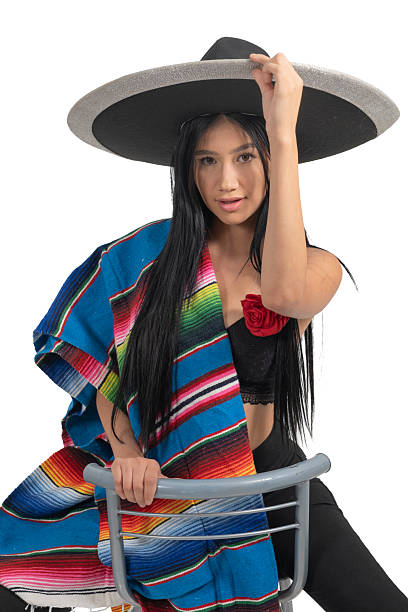 Black-haired model posing for a photo in traditional Mexican attire in a studio setting with a white background.
