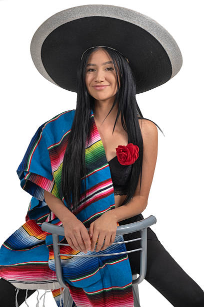 Black-haired model posing for a photo in traditional Mexican attire in a studio setting with a white background.