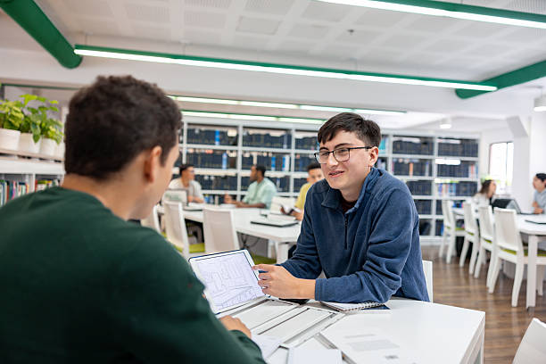 Architecture student showing a design to his friend while studying at the library using a digital tablet