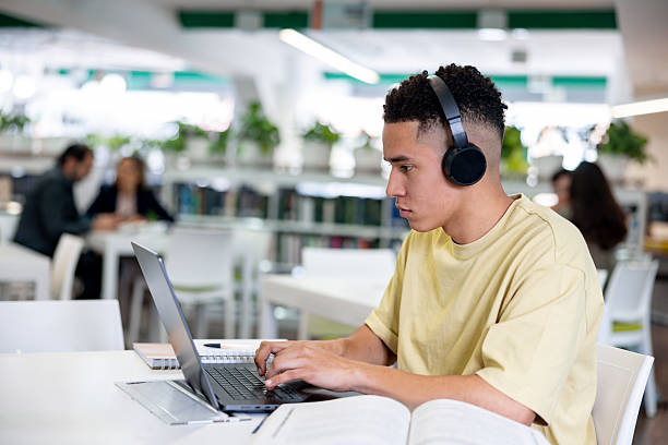istock College student studying at the library using his laptop and headphones 2226386018