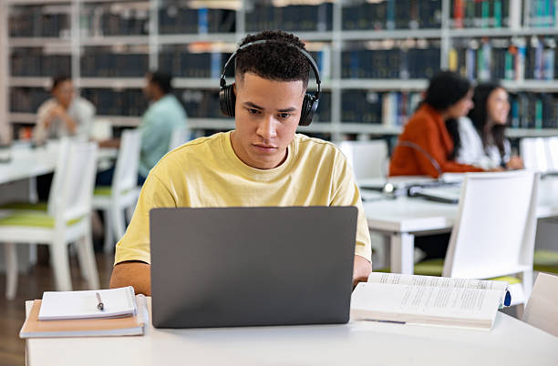 istock University student using his laptop and headphones while studying at the library 2226386022