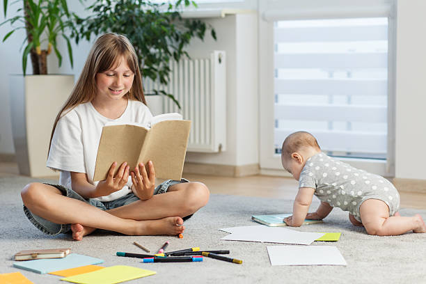 istock Older sister reading while baby crawls nearby on floor. Preparing for school. 2226388209