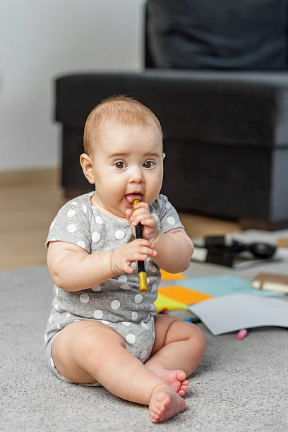 Cute baby chewing on marker while sitting on carpet