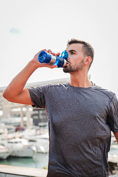 istock Vertical. Young handsome sportsman drinking energy water from bottle while resting after run workout. Male person of strong complexion having a break with a supplement and refreshing during training 2226389877