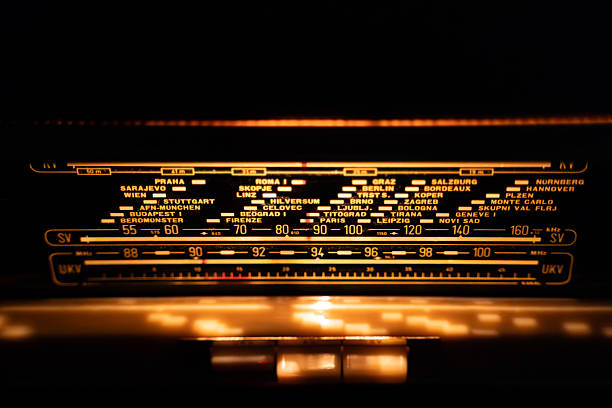 A close-up of a vintage radio dial glowing warmly with retro aesthetic, featuring frequency bands and European city names under soft, dim lighting.