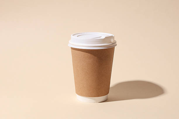 Craft cardboard disposable coffee cup on beige background with shadow. Minimalistic scene