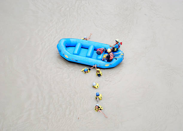 Pemalang, Indonesia. March 24, 2018. A group of diverse people is enjoying an adventurous white water rafting trip down a fast-flowing river. They are wearing safety helmets and life vests, paddling with enthusiasm. The rocky riverbanks and lush green trees add to the natural beauty of the scene.