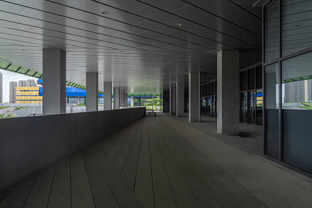 The image shows a spacious corridor inside a modern building. The corridor is poorly lit, with natural light coming in from the windows at the end. The floor is polished, reflecting light and enhancing the sense of openness. This scene is typical of a corporate building, hospital, or educational institution. Categories suitable for this image include architecture, interior design, corridors, modern buildings, office spaces, and public areas.