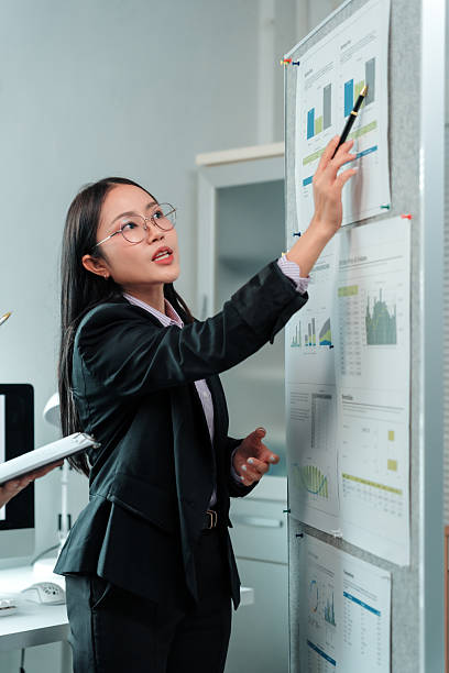 Young Asian businesswoman pointing at charts on a whiteboard during a presentation