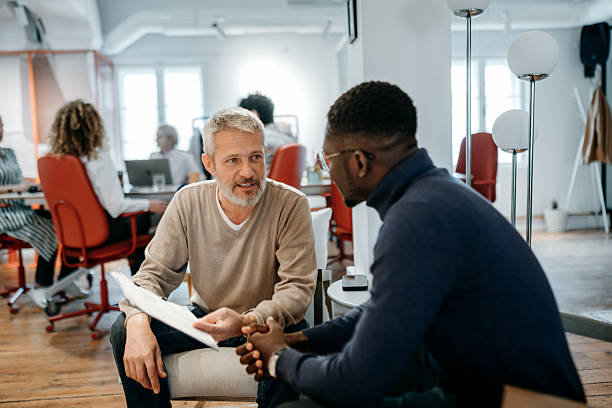 istock Two male colleagues talking while sitting in office lobby 2226416767