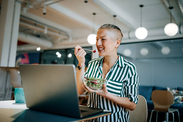 Woman working on laptop while having lunch in office cafeteria