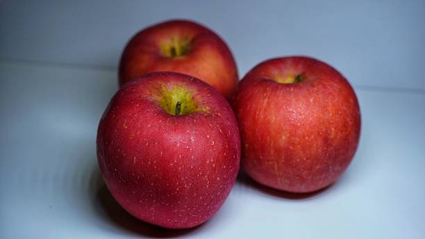 istock This image is a photograph of three red apples placed on a white surface. The apples are bright red with some yellowish speckles and a short stem at the top. 2226417756