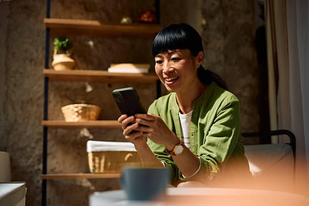 istock Asian woman using mobile phone and smiling while sitting on sofa at home 2226420370