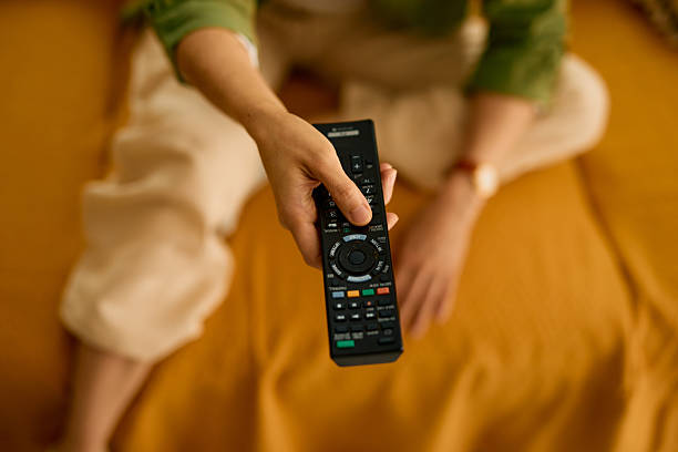 Woman holding a Sony TV remote control while sitting on a yellow sofa