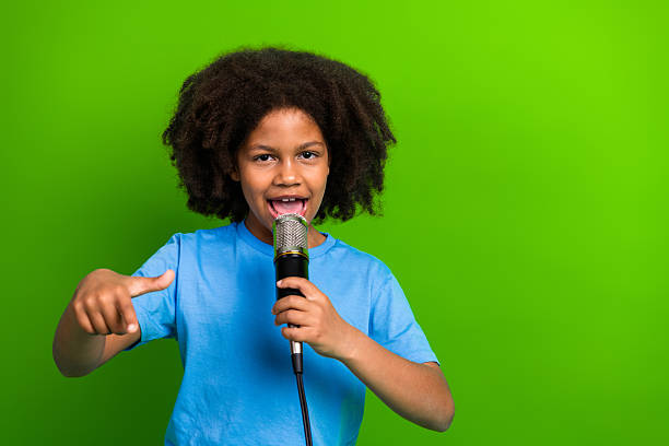 istock Young girl singing into microphone with enthusiastic expression against a vibrant green background wearing casual attire 2226420489