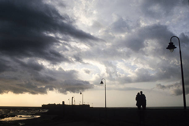 Brighton, UK - 2 January, 2025: a man uses his smart phone to photograph the view over Brighton Beach from a viewing platform. The man is thrown into silhouette due to the sunset.
