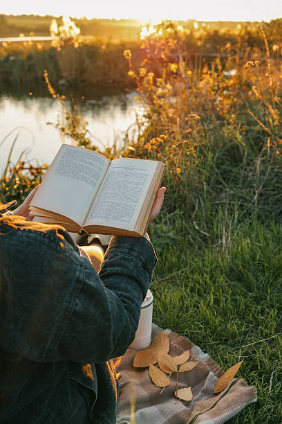 istock Girl by the river reading a book, beautiful sunset 2226423592