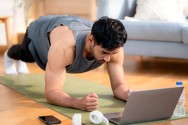 istock Young asian man doing plank exercise in living room at home while watching online workout tutorial on laptop with endurance and motivation, man training plank on yoga mat, digital fitness lifestyle. 2226425322