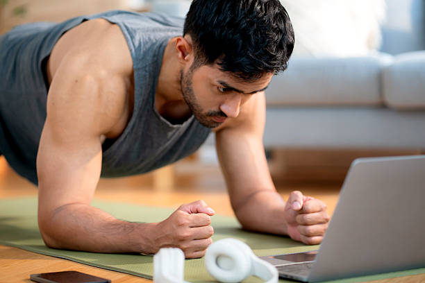 istock Young asian man doing plank exercise in living room at home while watching online workout tutorial on laptop with endurance and motivation, man training plank on yoga mat, digital fitness lifestyle. 2226425374