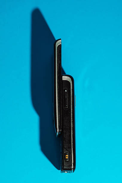 Retro slider phone standing upright on cyan paper with sharp shadow. Minimalist Y2K layout. High quality photo