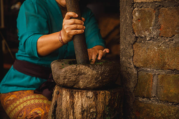 A close-up view of a traditional stone mortar used by a woman to pound herbs. The scene captures cultural authenticity and culinary traditions, emphasizing a rustic and natural ambiance. The composition highlights the hands at work, creating a vivid representation of craftsmanship and traditional practices.