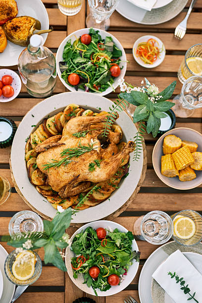 A beautifully arranged rustic outdoor meal with roasted chicken, fresh salads, grilled vegetables, and drinks on a wooden table. Perfect for a gathering in nature.