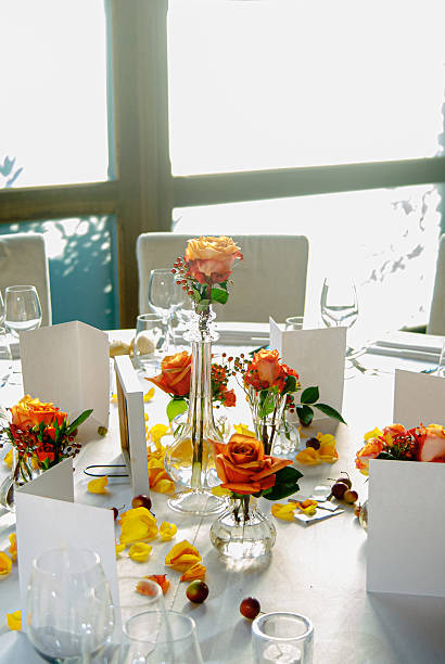 Elegant table setting with yellow roses in vases, petals scattered, and blank cards in a naturally lit ambiance, conveying a sense of refinement, serenity, and preparation for a special event.