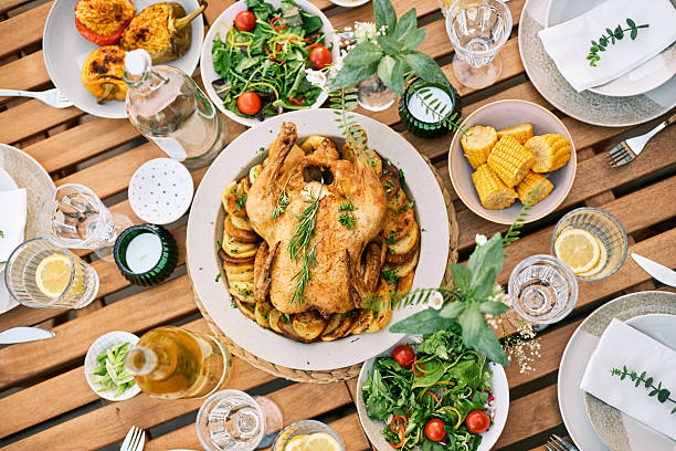 Beautifully set outdoor meal with grilled chicken, fresh vegetables, corn, and refreshing drinks on a wooden table. Perfect for a summer gathering.
