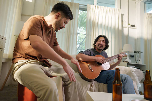 istock Two Asian men taking turns strumming acoustic guitar, enjoying drinks and conversation in a relaxed living room 2226430123