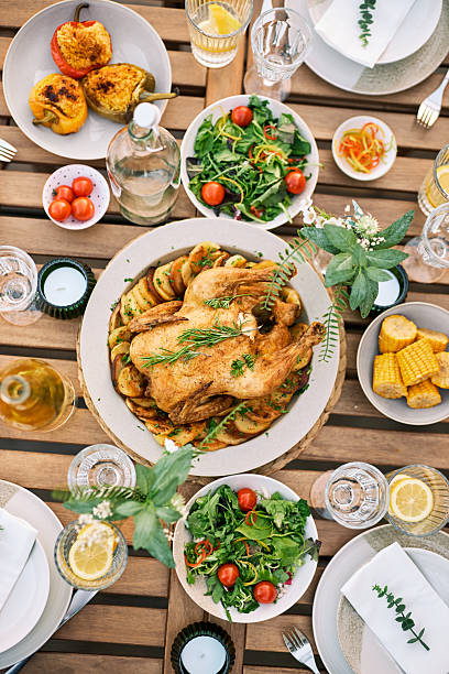 A beautifully arranged outdoor lunch table with roasted chicken, fresh salads, grilled vegetables, and corn on a wooden table, perfect for a nature getaway.