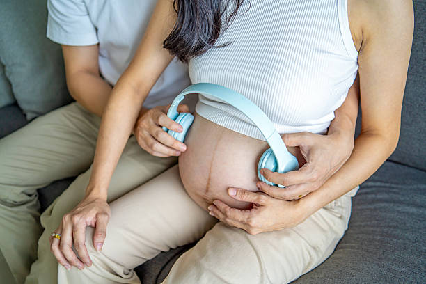 A tender moment as a loving husband places wireless headphones on his pregnant wife's tummy, sharing soothing music with their unborn baby to foster early bonding