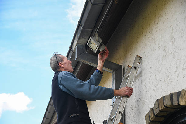 istock Professional electrician installing LED floodlight on ladder, working on house exterior beneath roof gutter, providing enhanced outdoor illumination and security measures 2226436896
