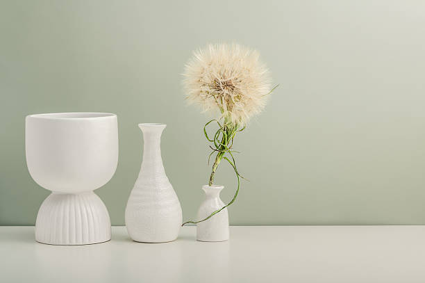 Three ceramic vases and a large dandelion on a white table against an olive wall.