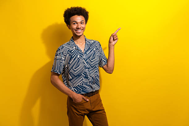 istock Charismatic young man pointing towards a direction with a cheerful expression against a bright yellow background in a stylish outfit 2226439221