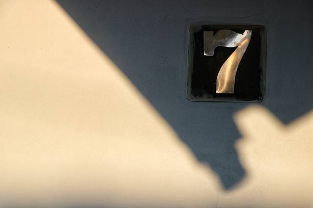 The number 7 on a wall illuminated by sunlight and shadows.