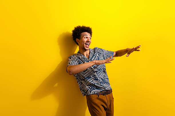 Charismatic young man making expressive gestures against a vibrant yellow background, perfect for lifestyle and fashion themes