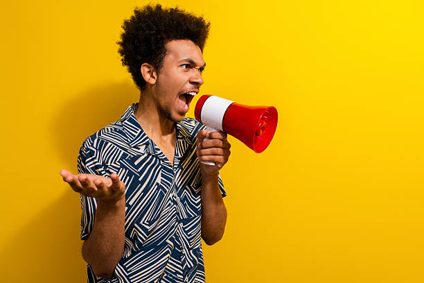istock Energetic young man shouting into a megaphone against a vibrant yellow background expressing enthusiasm and charisma 2226440215