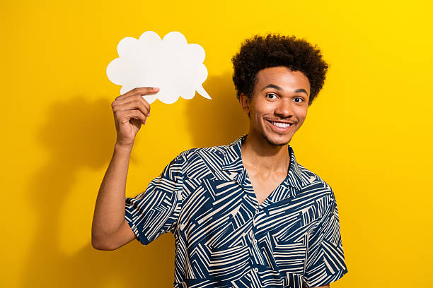 istock Charismatic man with afro haircut posing with a white speech bubble, expressing positivity against a vibrant yellow background 2226440239