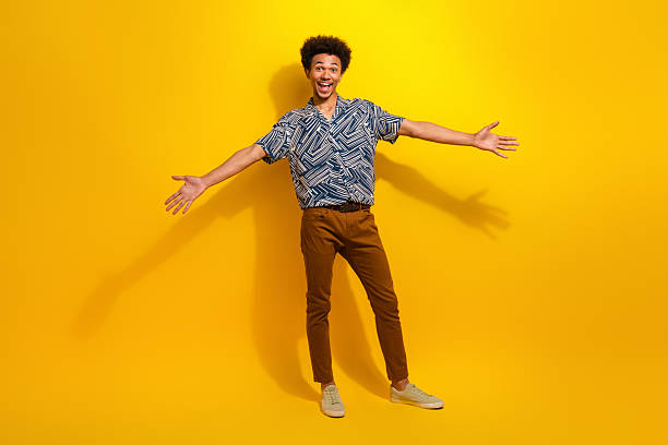 istock Happy young man with a cheerful expression standing in front of a bright yellow background, spreading arms wide 2226440278