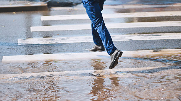 istock Businessman carefully jumping over a puddle on a crosswalk, avoiding getting his shoes wet 2226448849