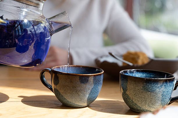 istock Pouring tea carefully and gracefully into elegant cups that rest on a sunny table setting 2226450480