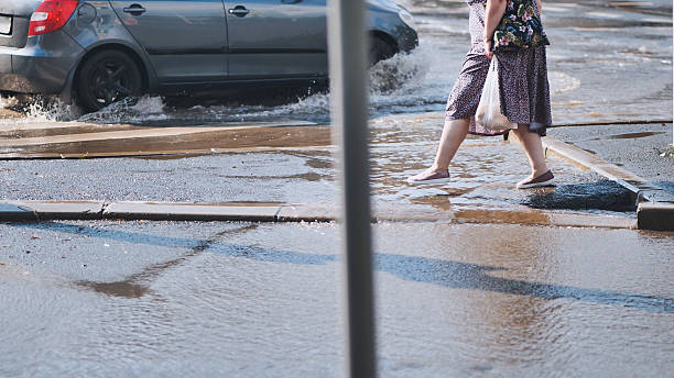 istock Commuter walking through large puddle on pedestrian crossing after heavy rainfall, with car splashing water nearby 2226450962