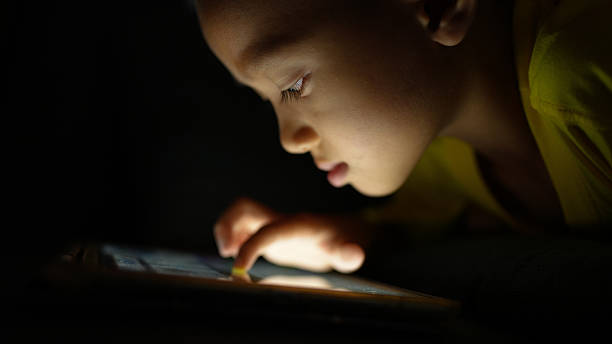istock Child focused on tablet screen in dimly lit environment, showcasing curiosity and engagement. soft glow from device highlights child features, creating warm and intimate atmosphere 2226452065